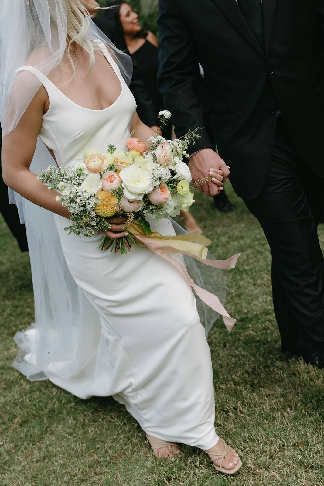 Close-up of the bride's radiant bouquet, elegantly held as she walks hand in hand with her new husband.