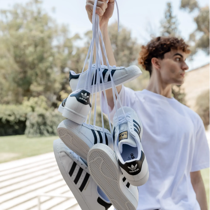 male model holding several pairs of adidas superstars by laces