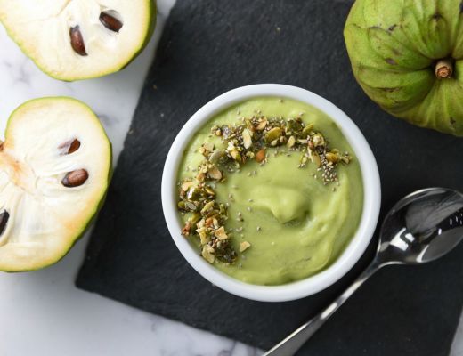Bowl of green cherimoya smoothie garnished with nuts, surrounded by cherimoya fruit.