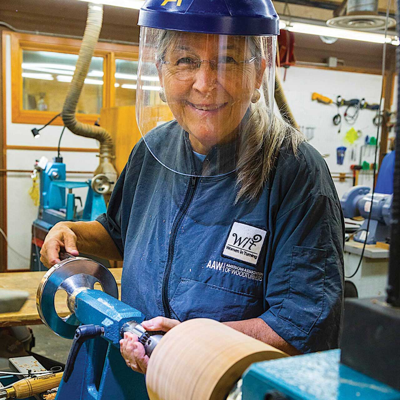 Woman working with a lathe, wearing safety gear in a workshop.