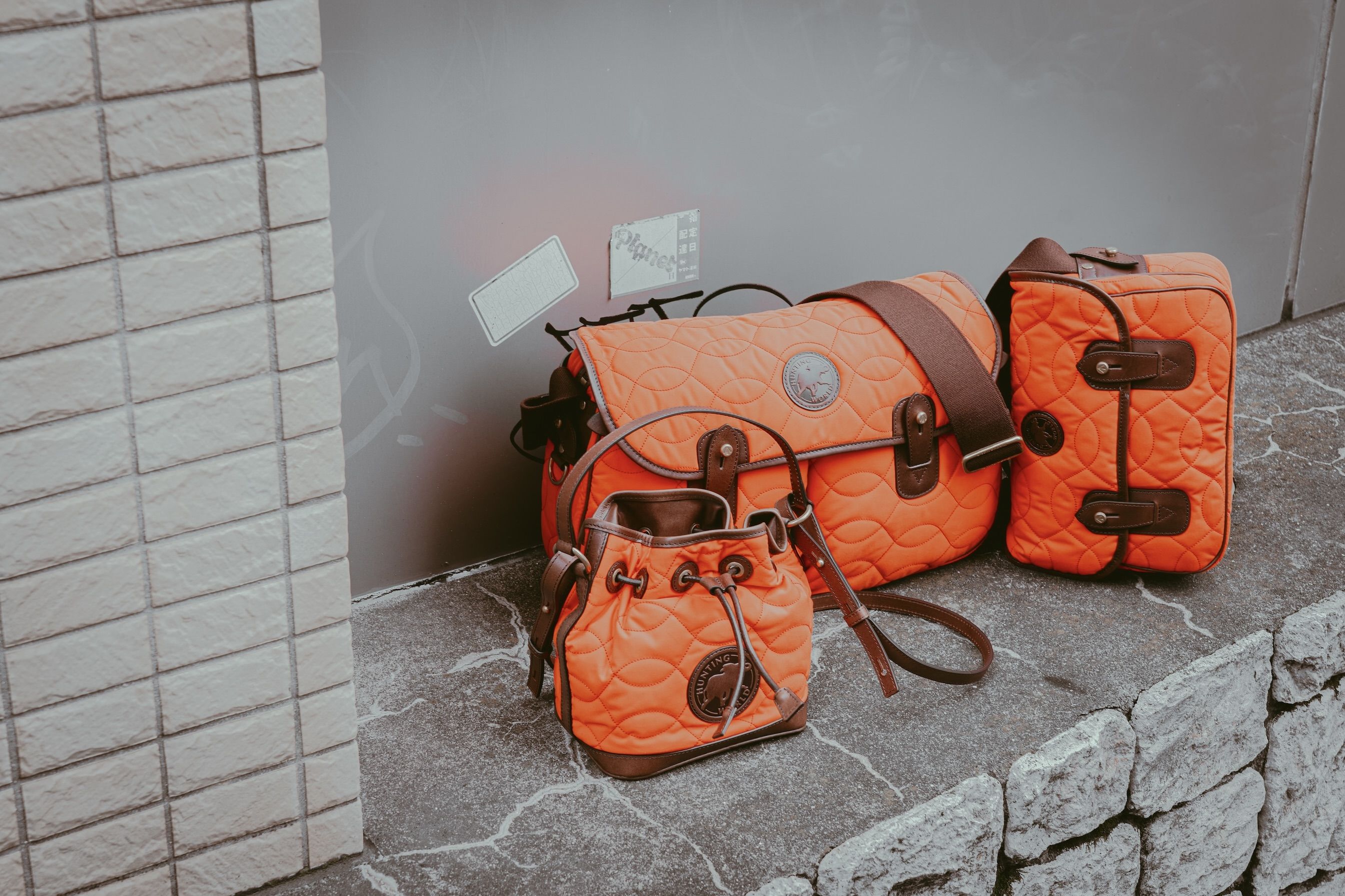 Three orange bags on a stone surface against a gray wall.