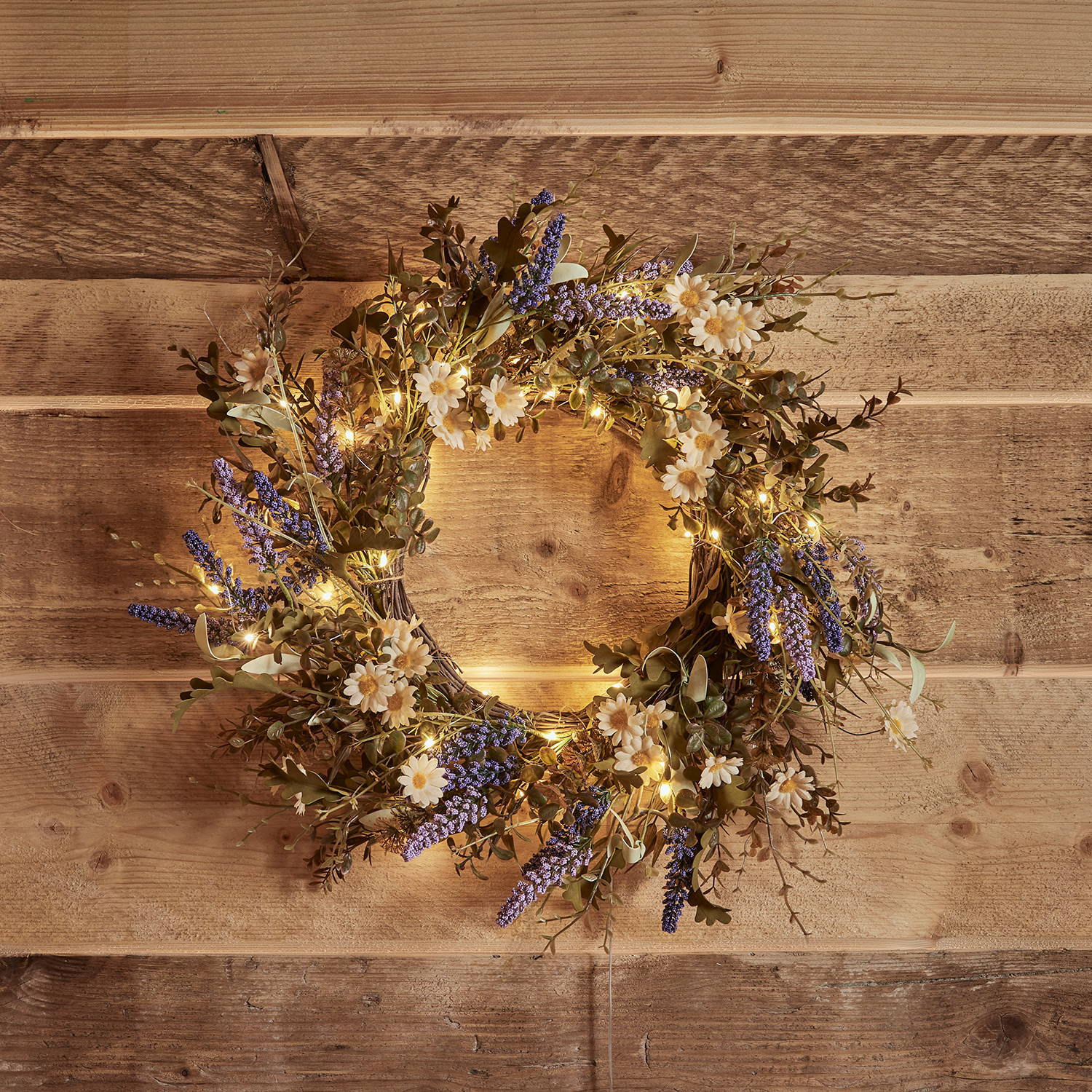 Meadow wreath with spring flowers and micro-lights against a wooden background.