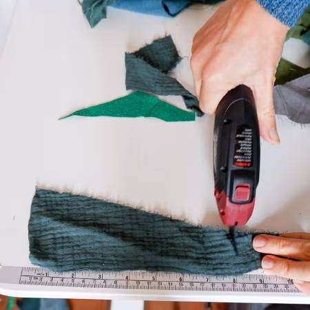 cutting fabric scraps on a table with electric fabric scissors and a ruler tape that is attached to the table