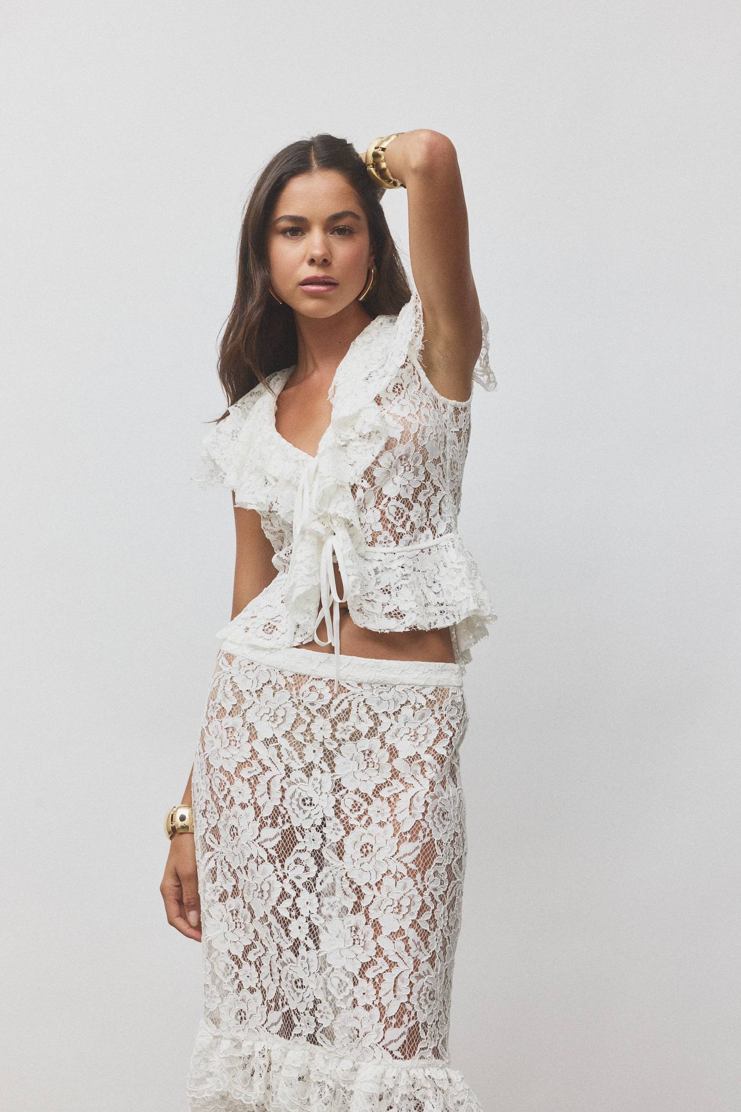 Model wearing a white lace outfit with ruffles, posing against a plain background.