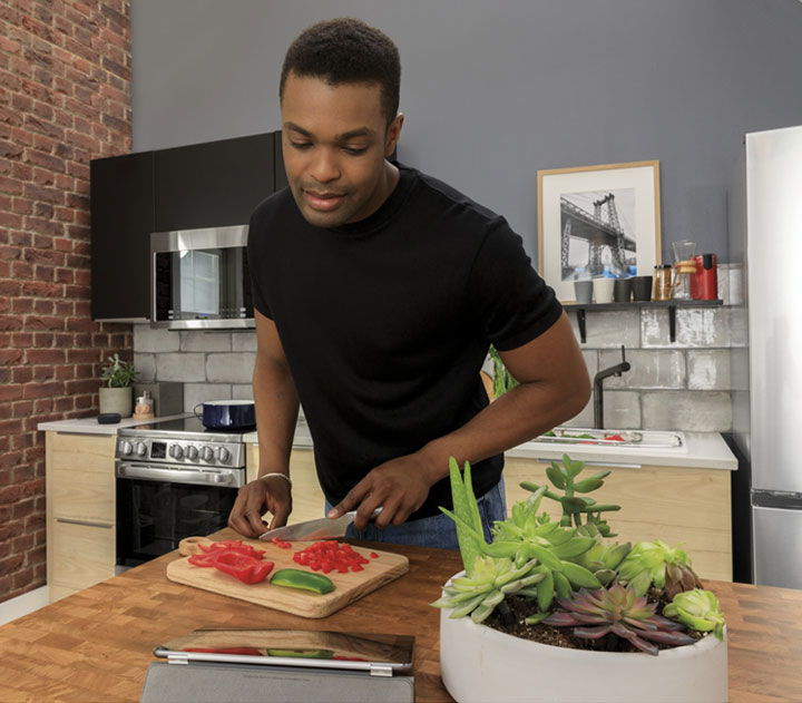 Person slicing vegetables in a modern kitchen with plants on the table.
