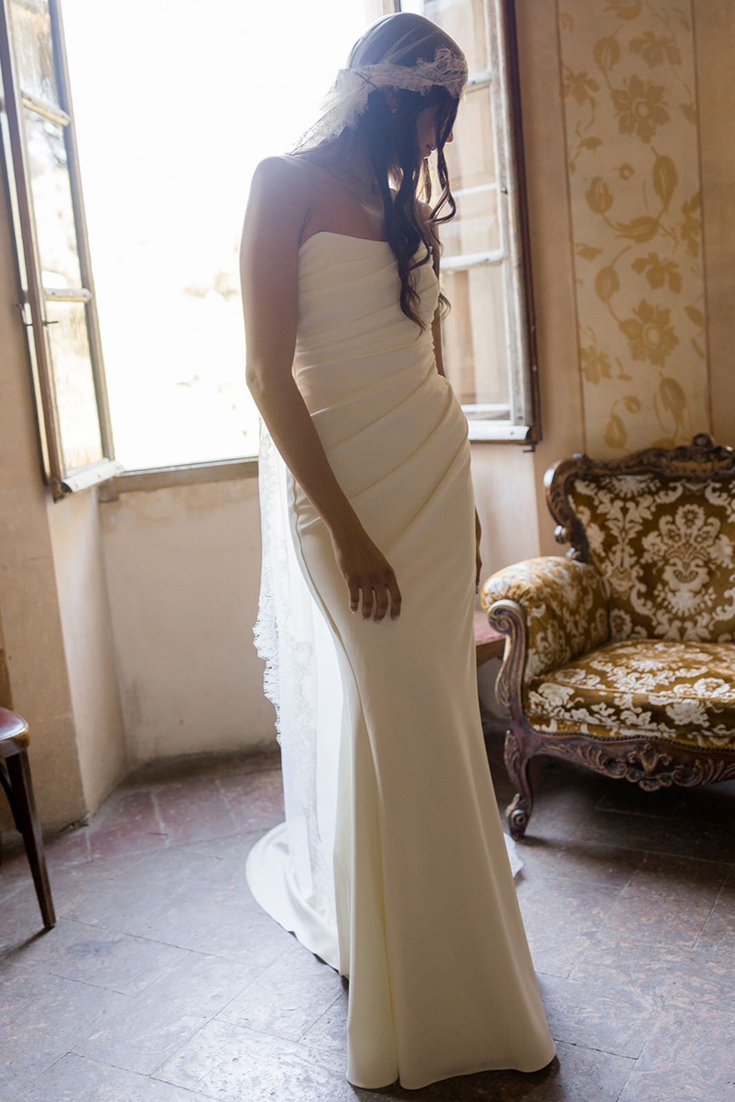 Bride in a white dress standing near a window.