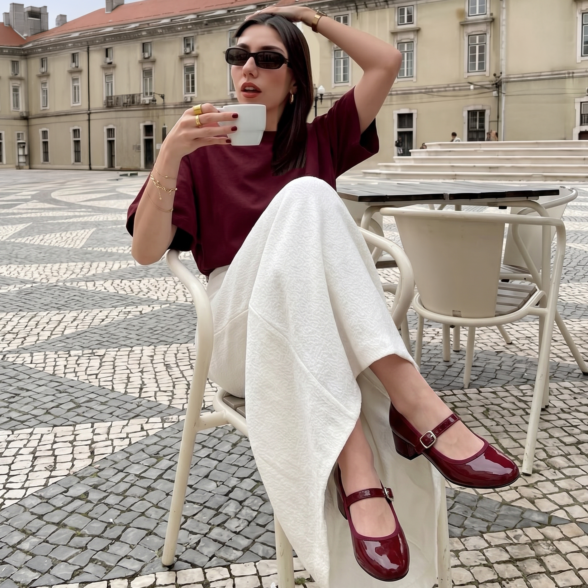 Person sitting on a chair, wearing sunglasses and a maroon shirt, holding a phone.