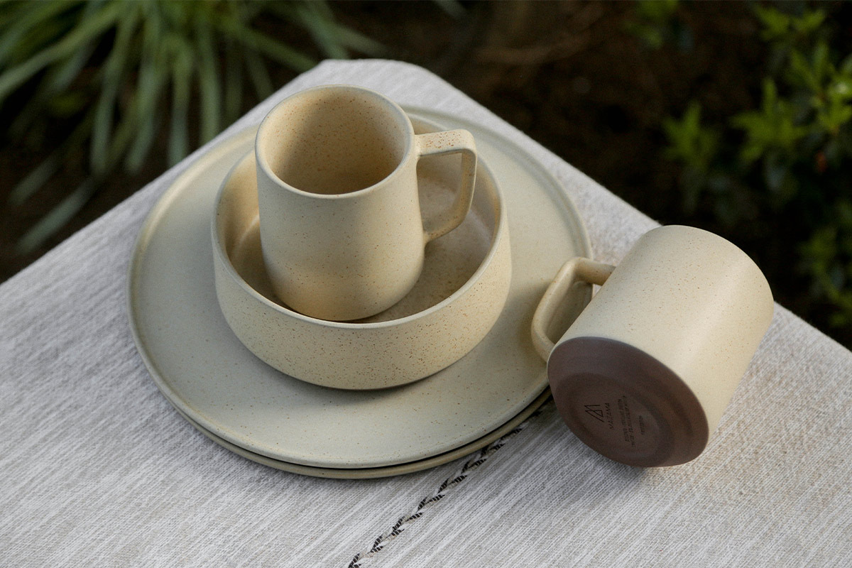 Collection of ceramic tableware on an outside table, including two plates, two mugs and a bowl.