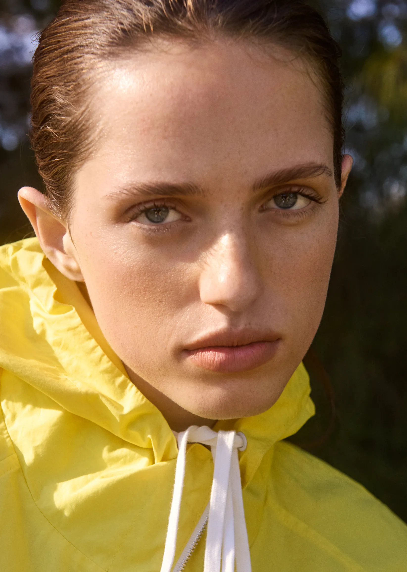 Young woman in a yellow raincoat with a serious expression.
