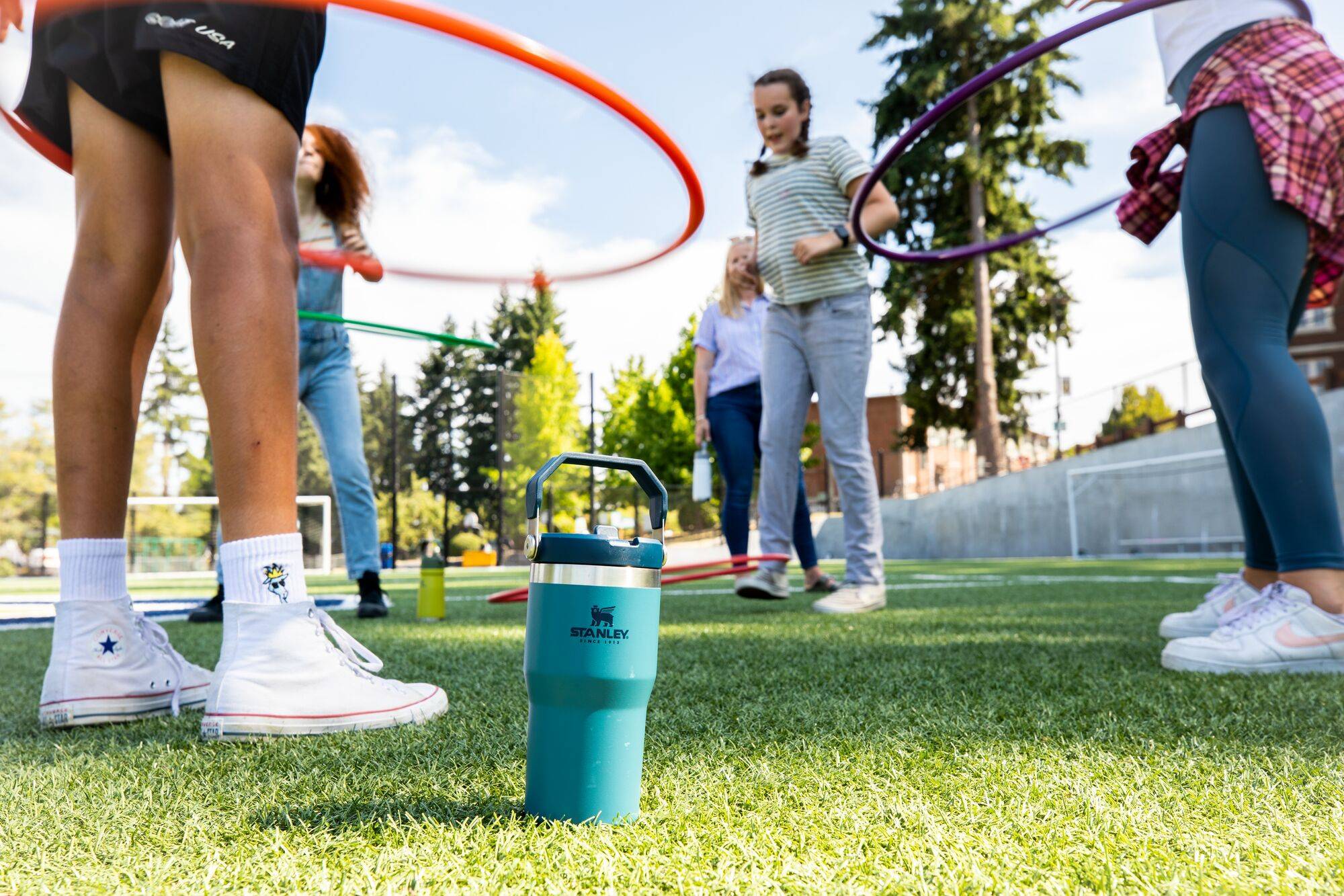 Kid hula hooping on playground with Stanley water bottles