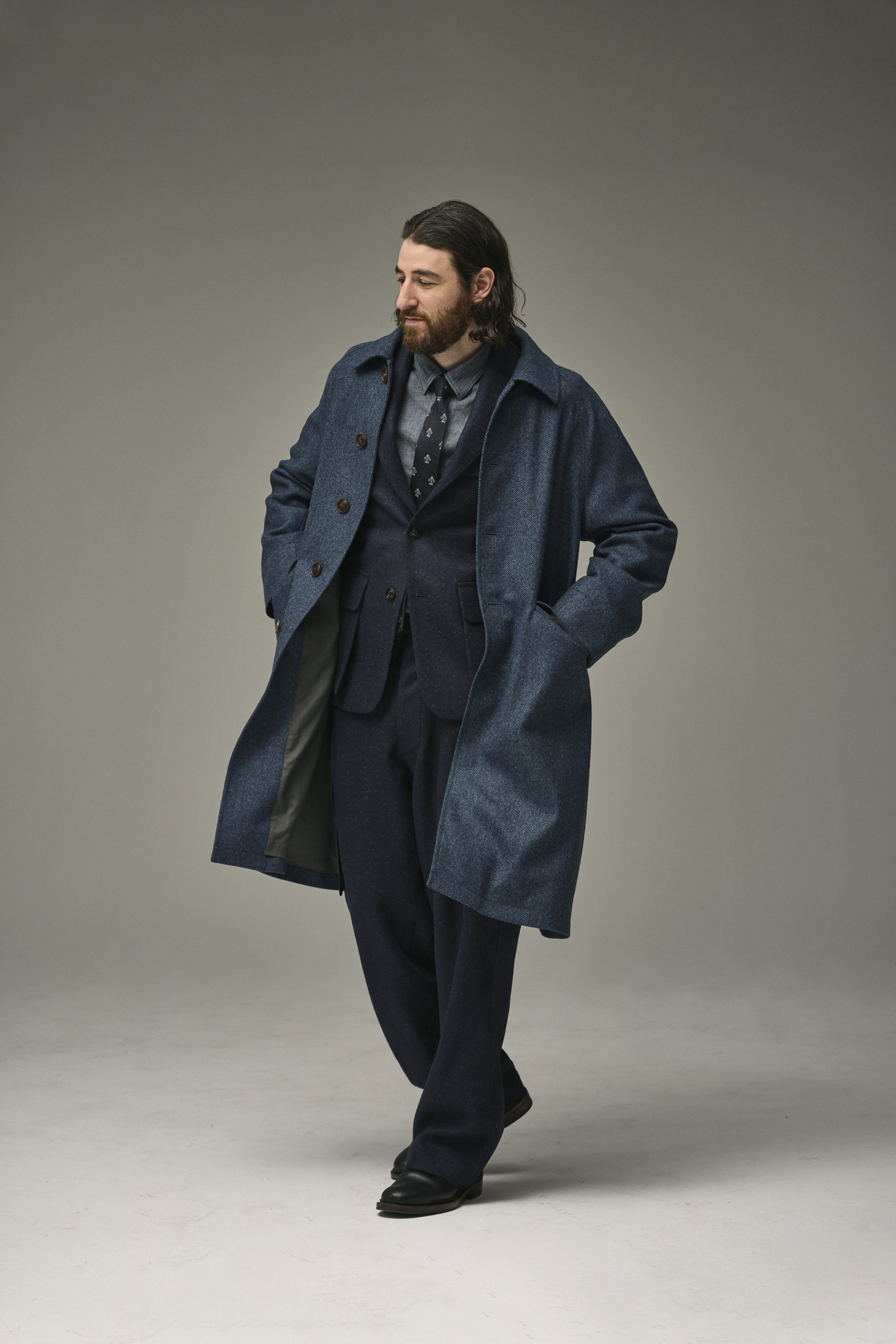 Man in a dark coat and suit, posing against a neutral background.