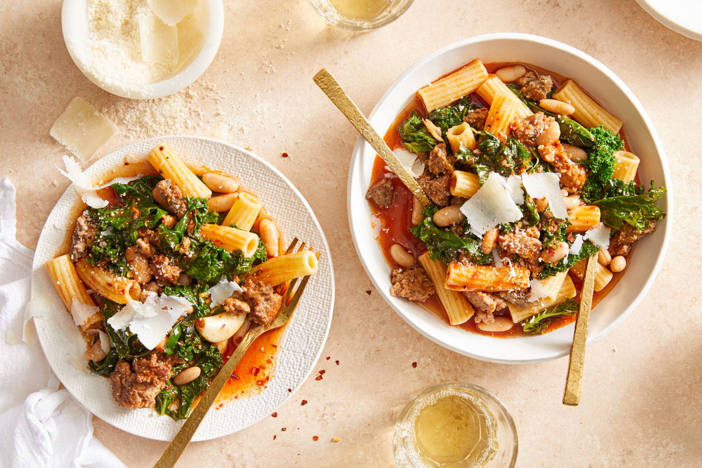 Two bowls of tortiglioni pasta in a red brothy soup with beans, kale and crumbled sausage