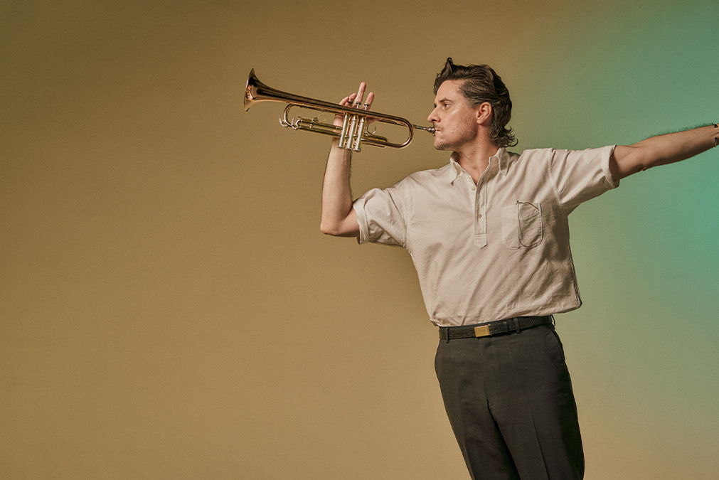 Person playing a trumpet, striking a dynamic pose against a plain background.