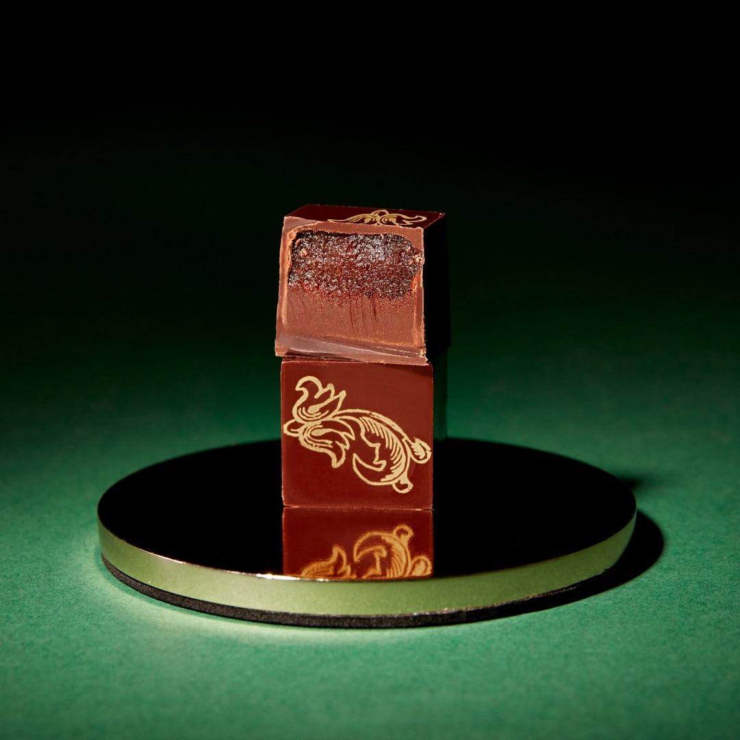 A chocolate cube on a reflective surface with decorative designs.