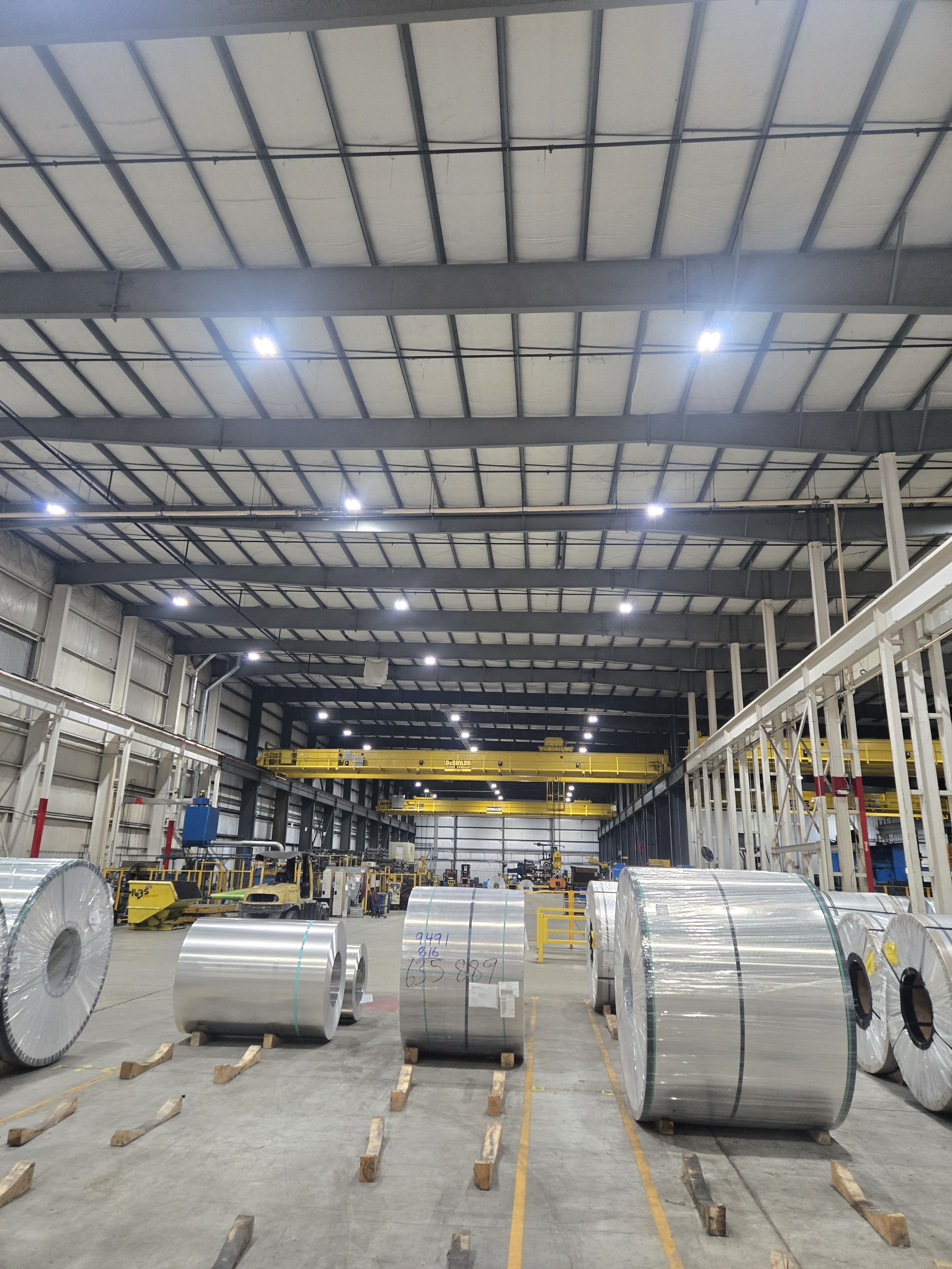 Coils of metal in a spacious industrial warehouse with high ceilings.