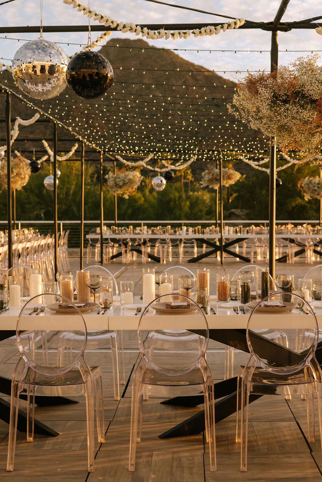 The outdoor wedding table is adorned with candles, and elegant place settings, while a sparkling disco ball overhead adds a touch of playful glamour to the scene.