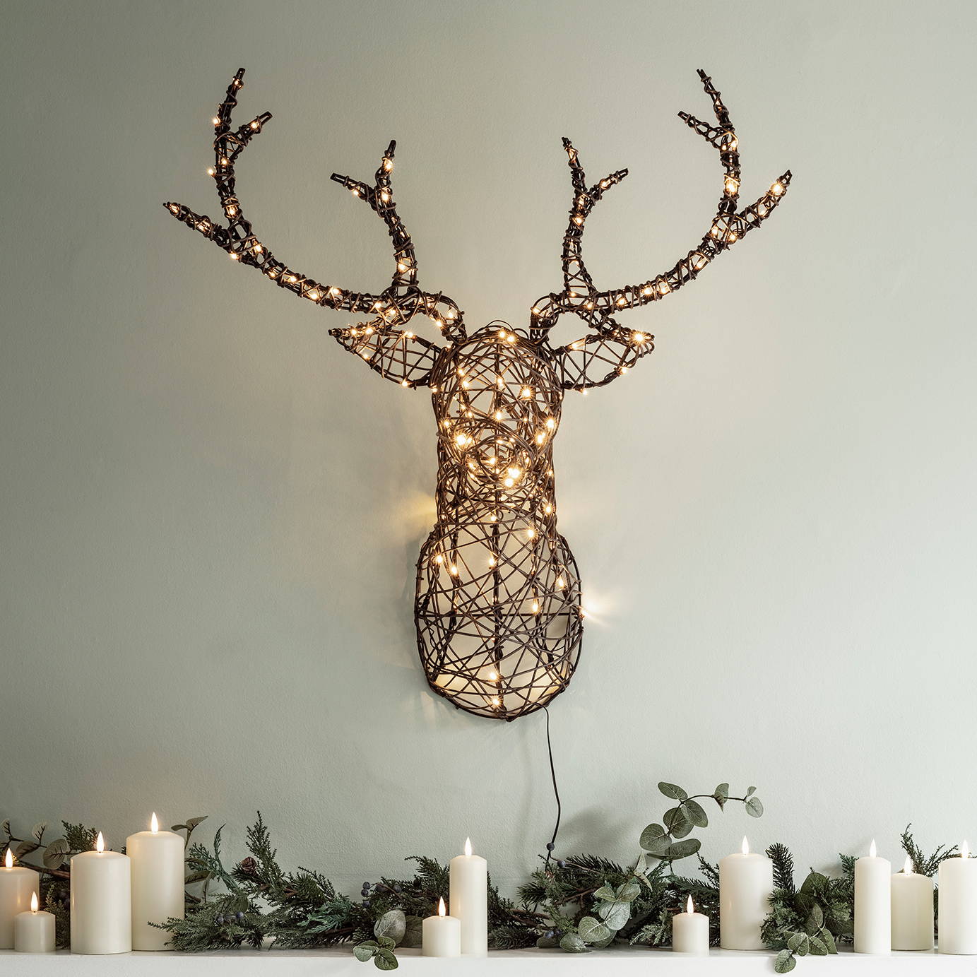 Rattan stag head silhouette Christmas light handing above a fireplace decorated with a Christmas garland and candles