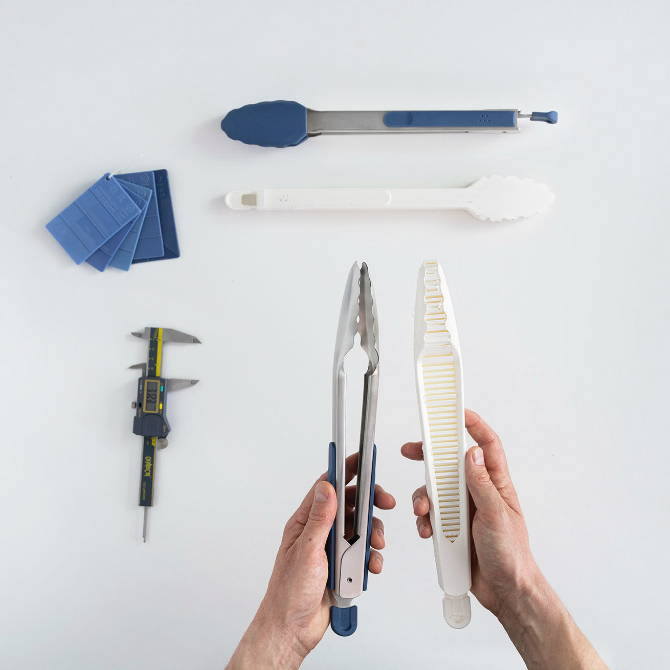 Hands holding a set of Misen Tongs and a 3D printed prototype on a white background. Calipers and color swatches are also visible.