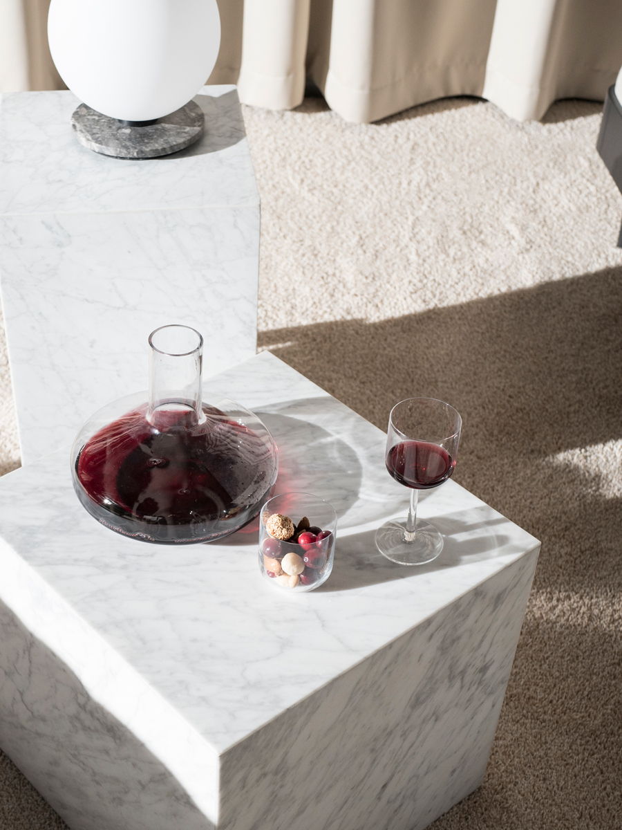 A marble Plinth table by Audo with a decanter, glass, and fruit bowl in soft lighting.