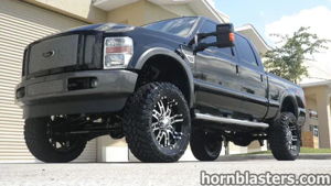 Low-angle front view of Wicked Customs's lifted black 2008 Ford F250 Super Duty with off-road tires in front of a garage