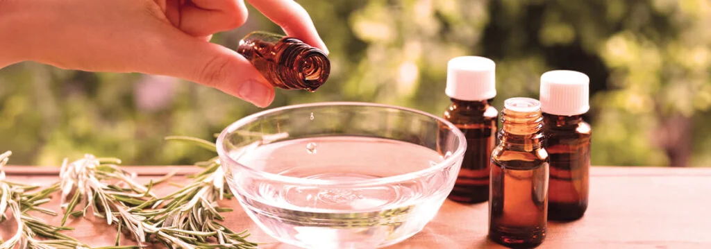 Person adding essential oil to a bowl of water, with brown bottles nearby.
