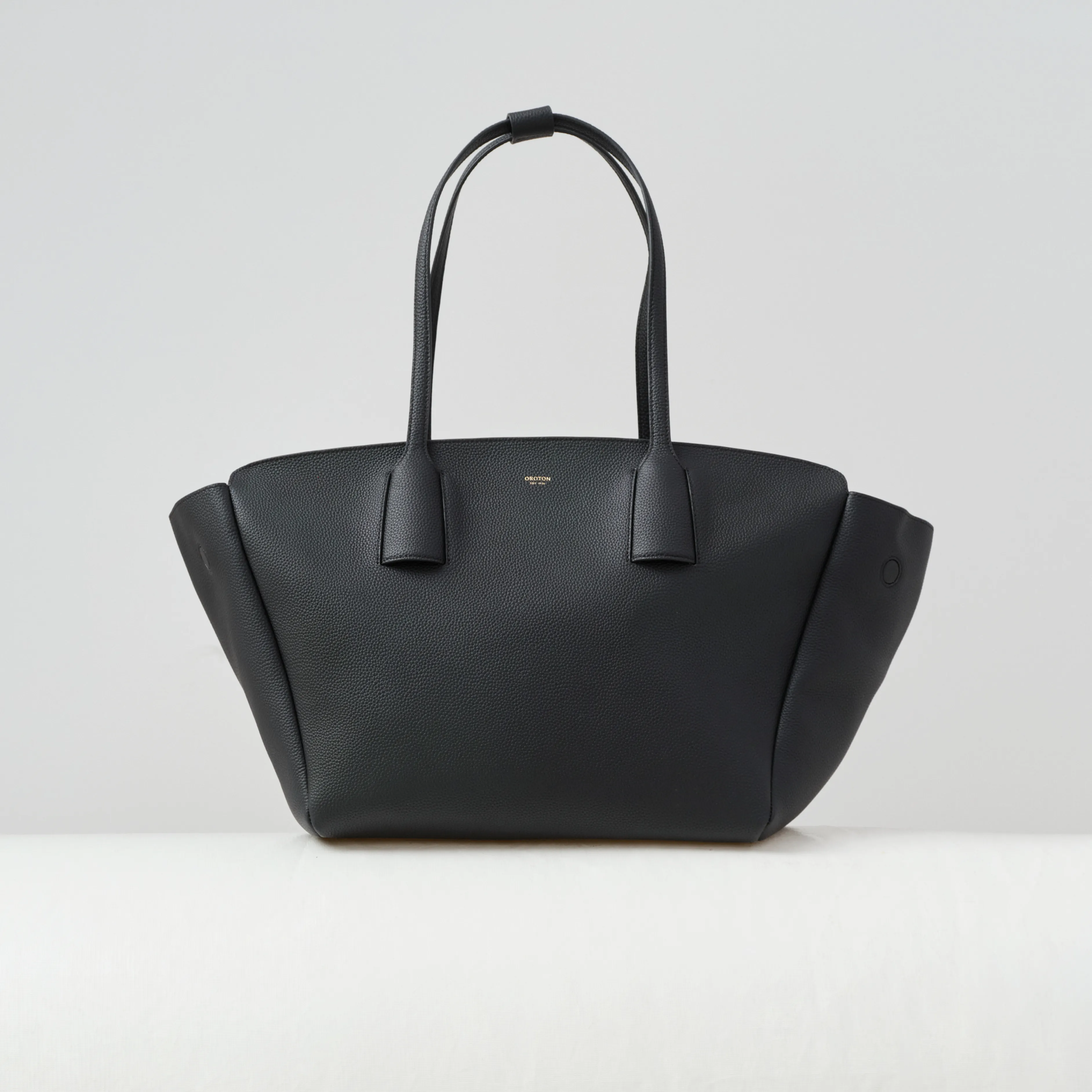 Black handbag with two handles against a plain background.