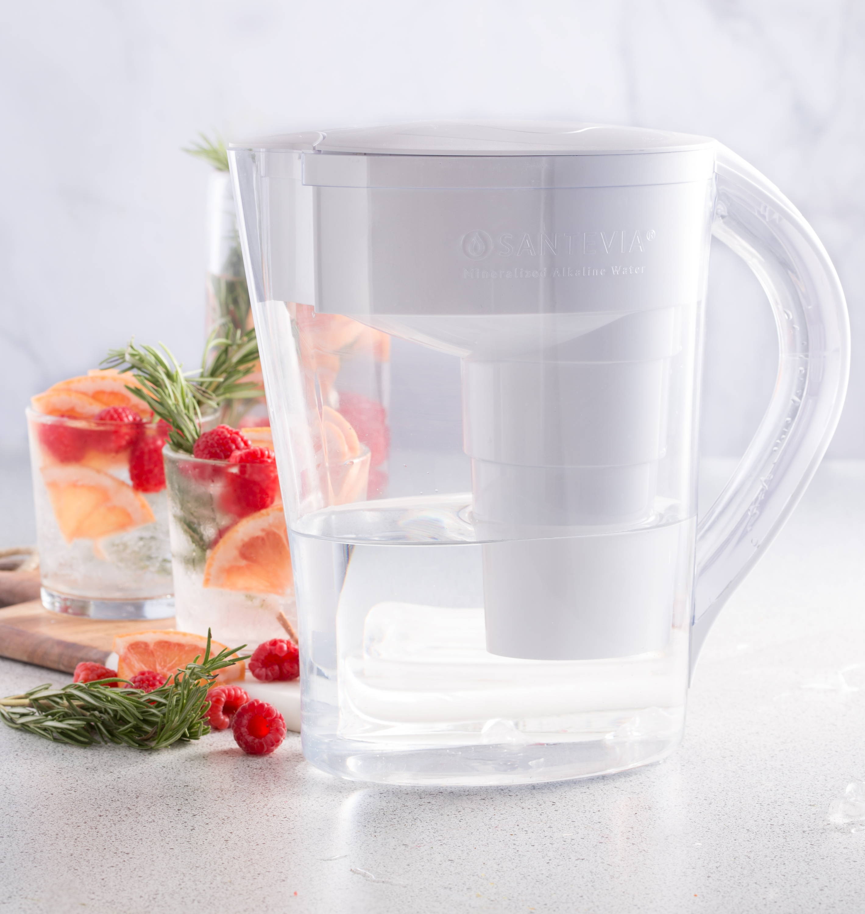 MINA Alkaline Pitcher with two glasses of water infused with rosemary, raspberries, and grapefruit