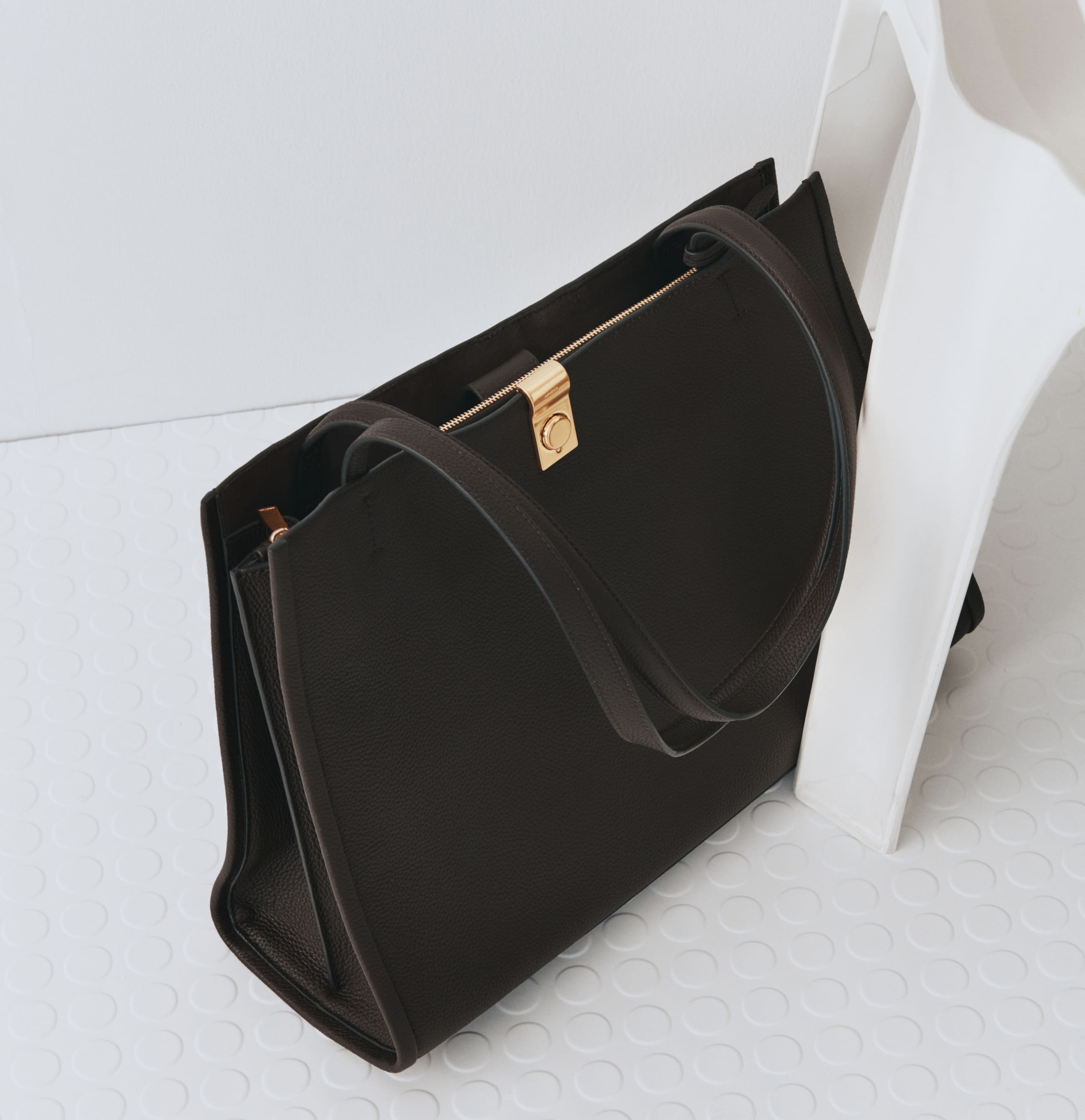 A black handbag resting beside a white object on a light background.