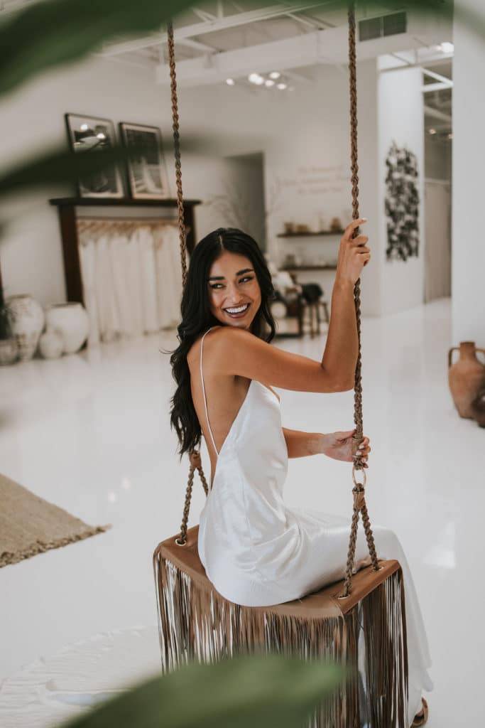 Femme sur une balançoire à pompons en cuir à l'intérieur de la boutique de robes de mariee, portant la robe Grace Loves Lace Oceania.