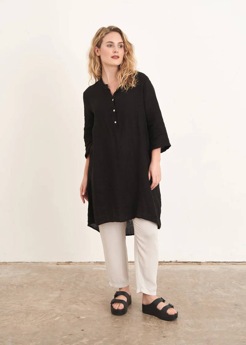 A model wearing a long black linen tunic top with off white trousers and black slides