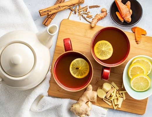 Two cups of tea with lemon, ginger, and cinnamon on a wooden board.