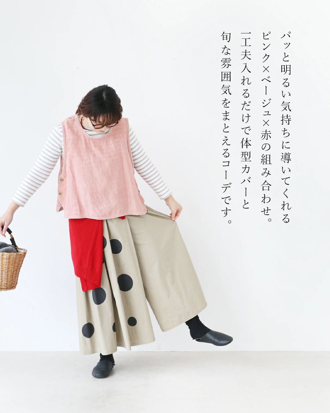 Woman in a pink top and polka dot pants holding a basket.
