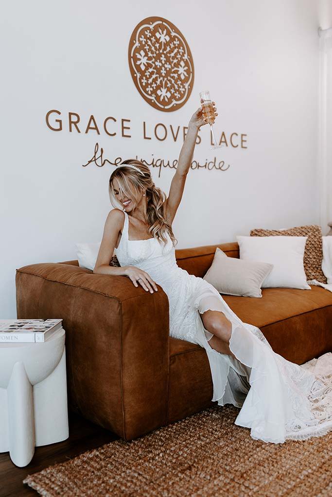 Braut im Grace Loves Lace Showroom mit Champagnerglas in der Hand