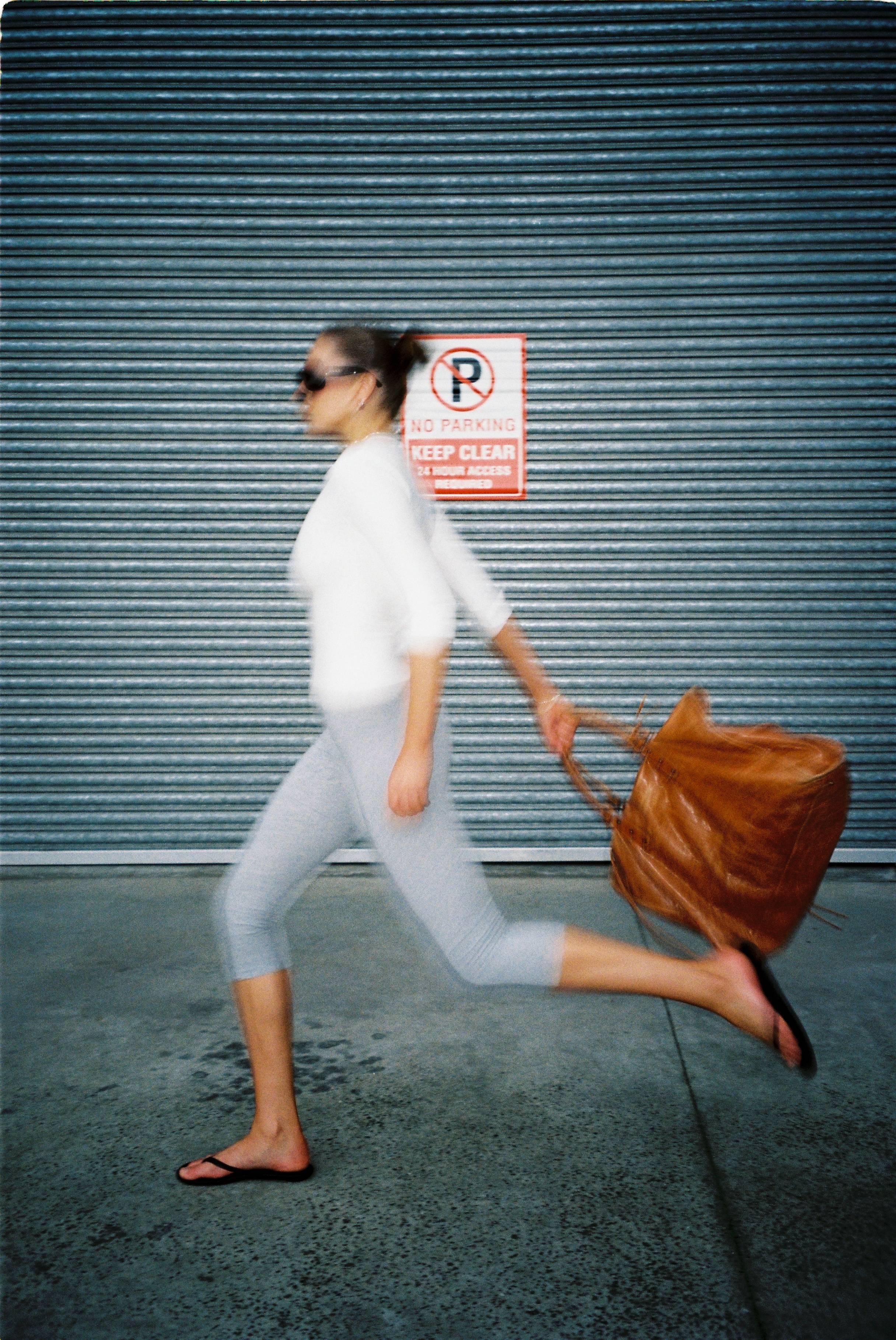 Woman running with a large bag in front of a metal door.