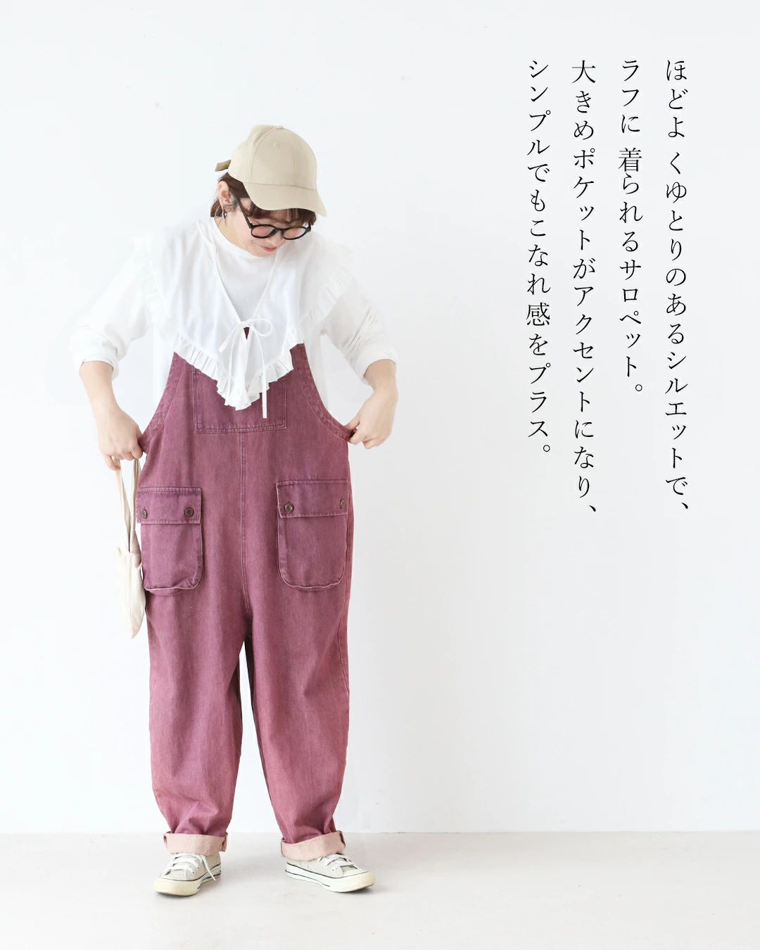 Person wearing a white top and pink overalls, standing against a white background.