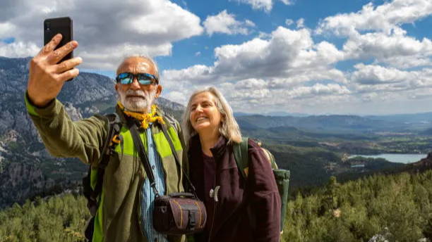 Older couple hiking and taking a selfie with mountains int the background