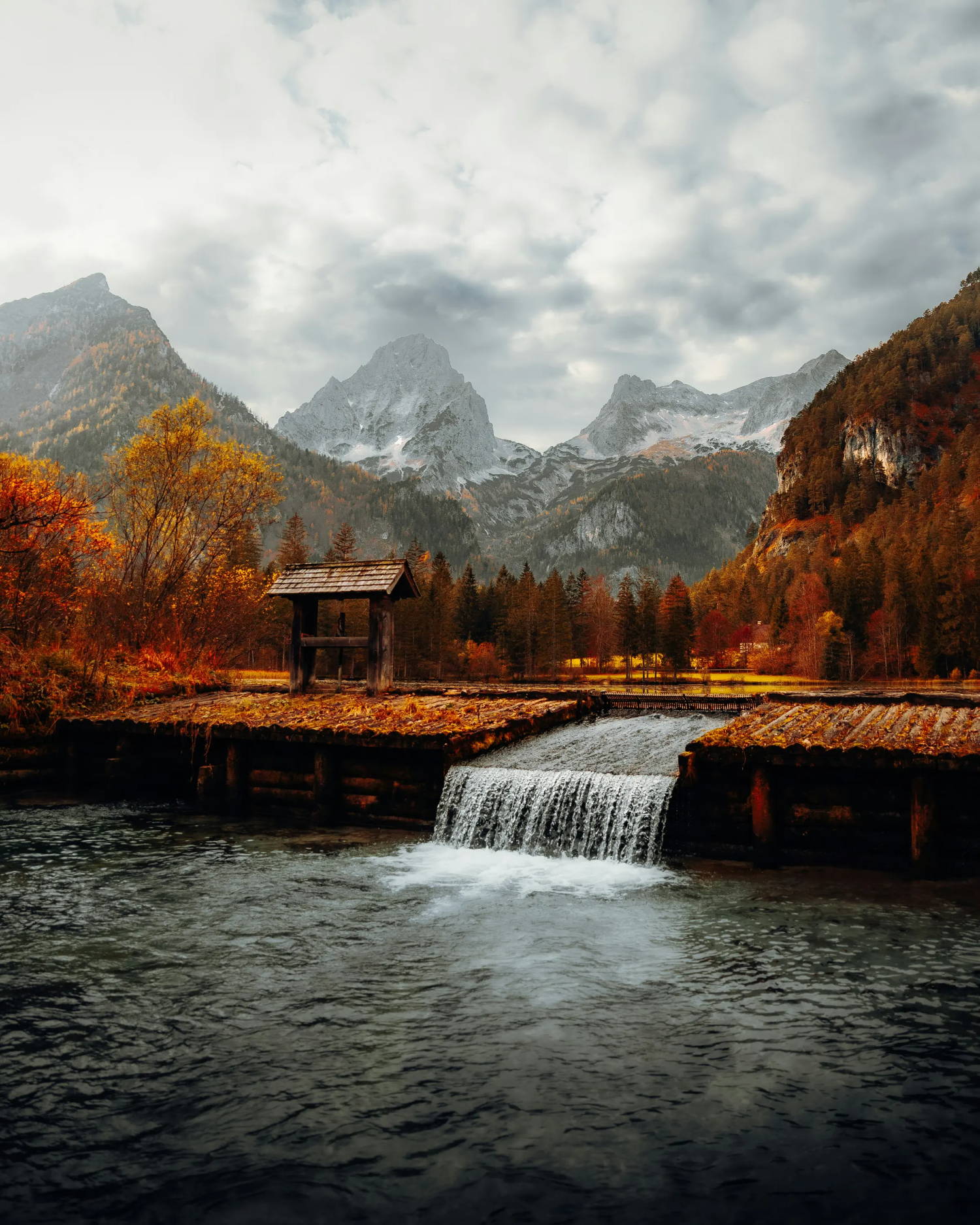 A mountain range with autumn-colored trees and a waterfall in the foreground