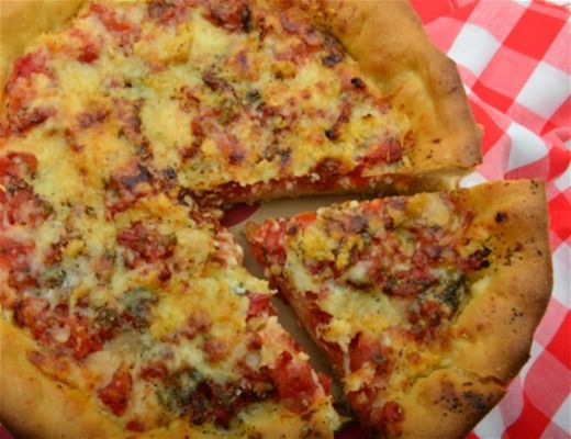 A freshly baked pizza with a slice removed on a checkered tablecloth.