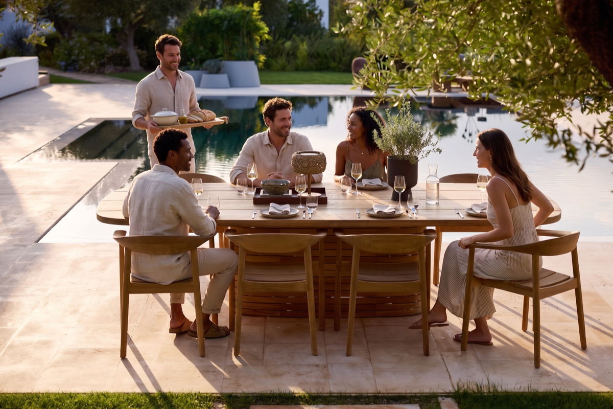 Guests gathered around an outdoor dining table beside a pool, showing a relaxed backyard dining area for entertaining. 