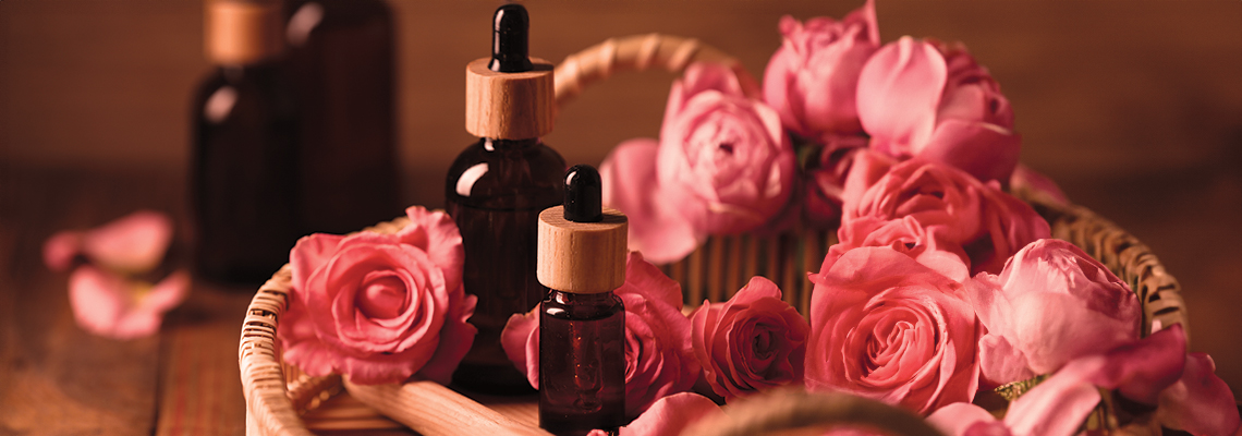 Bottles of essential oil surrounded by fresh pink roses in a basket.
