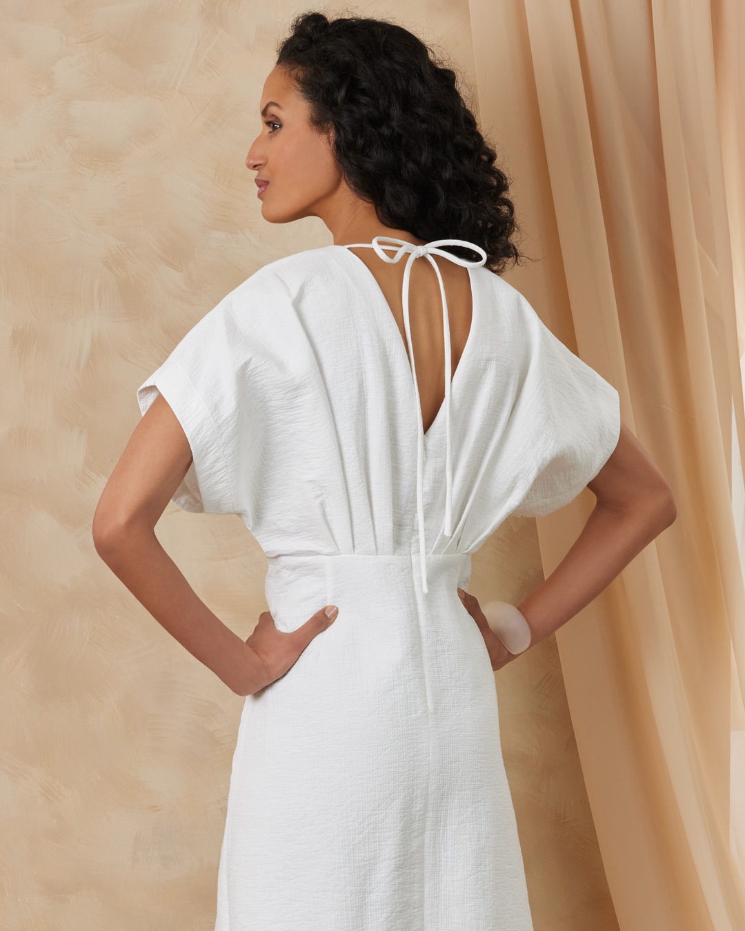 Woman in a white dress standing against a soft, neutral background.