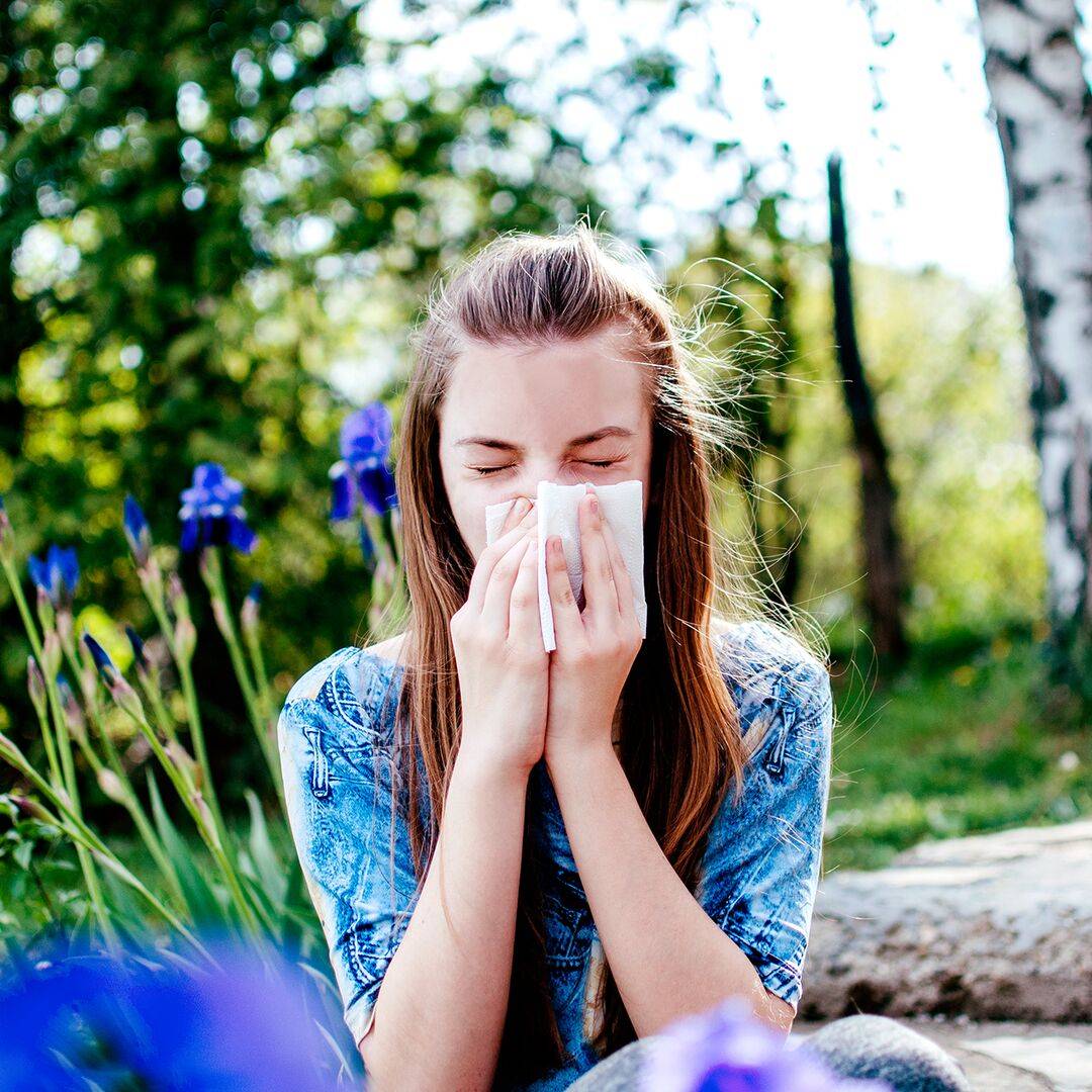 Une adolescente se mouche - il fait soleil et il y a des bouleaux derrière elle, elle a peut-être une allergie au pollen