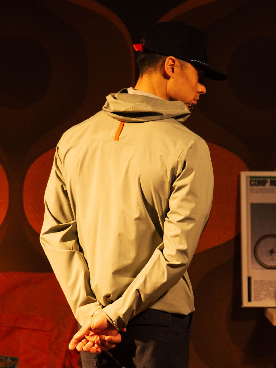 A person wearing a jacket and cap, looking back with hands clasped.