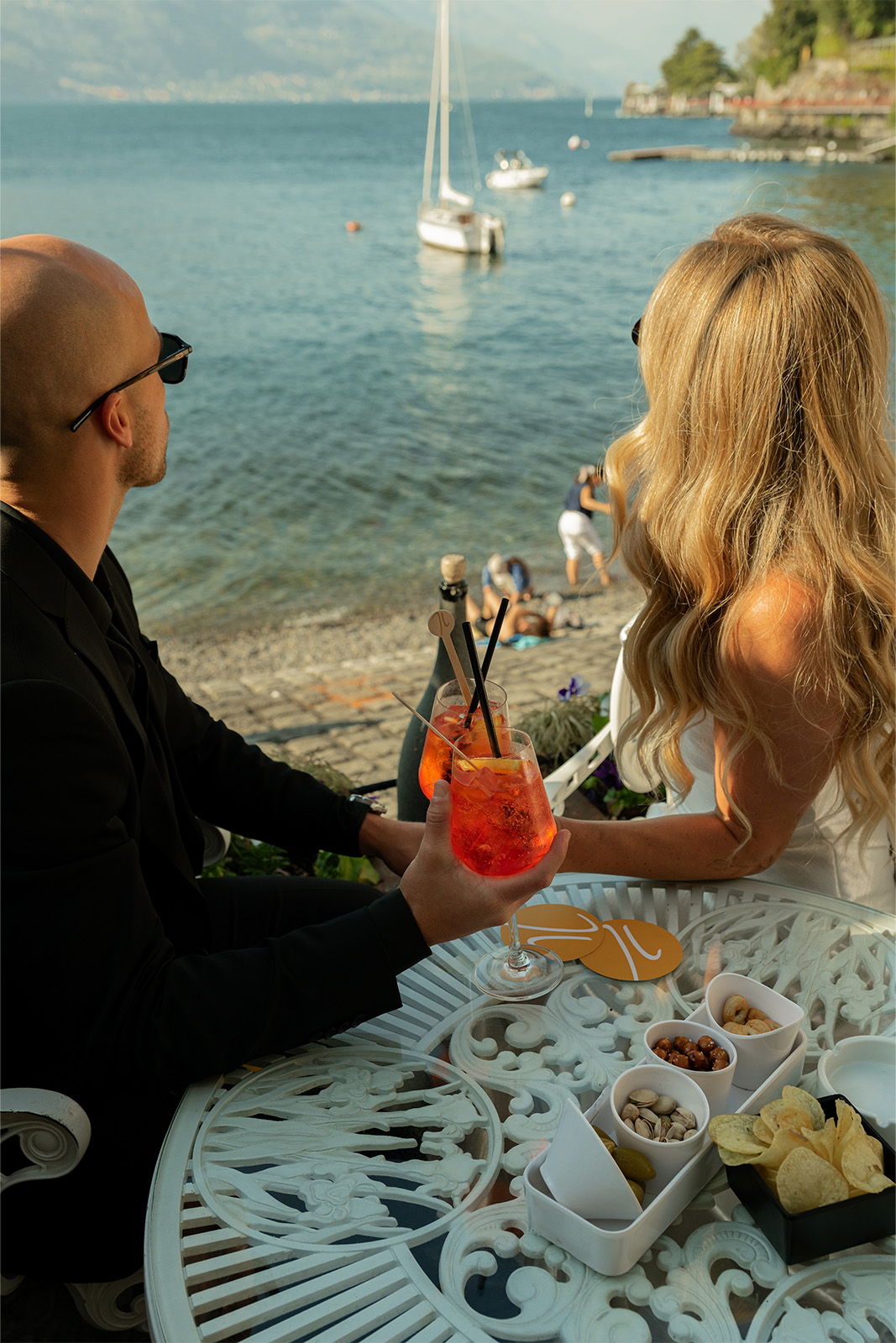 A couple enjoying drinks by the seaside with snacks on a table.