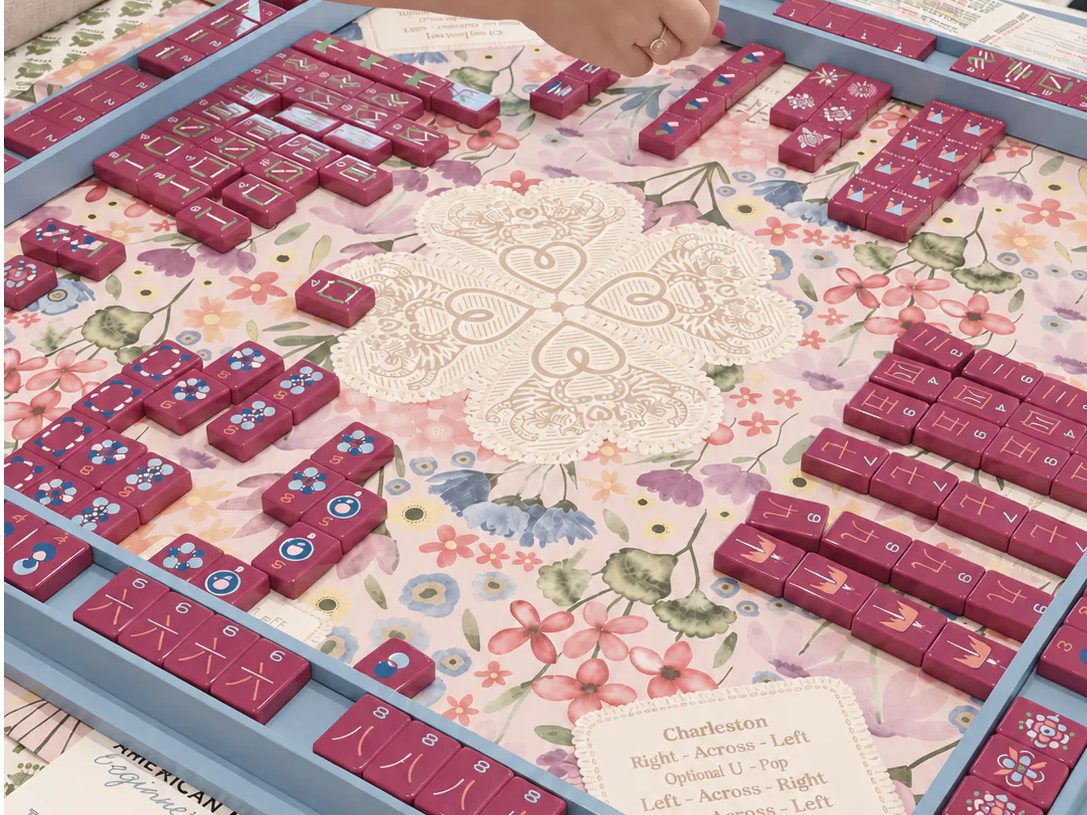 A person playing a game with colorful tiles on a floral tablecloth.