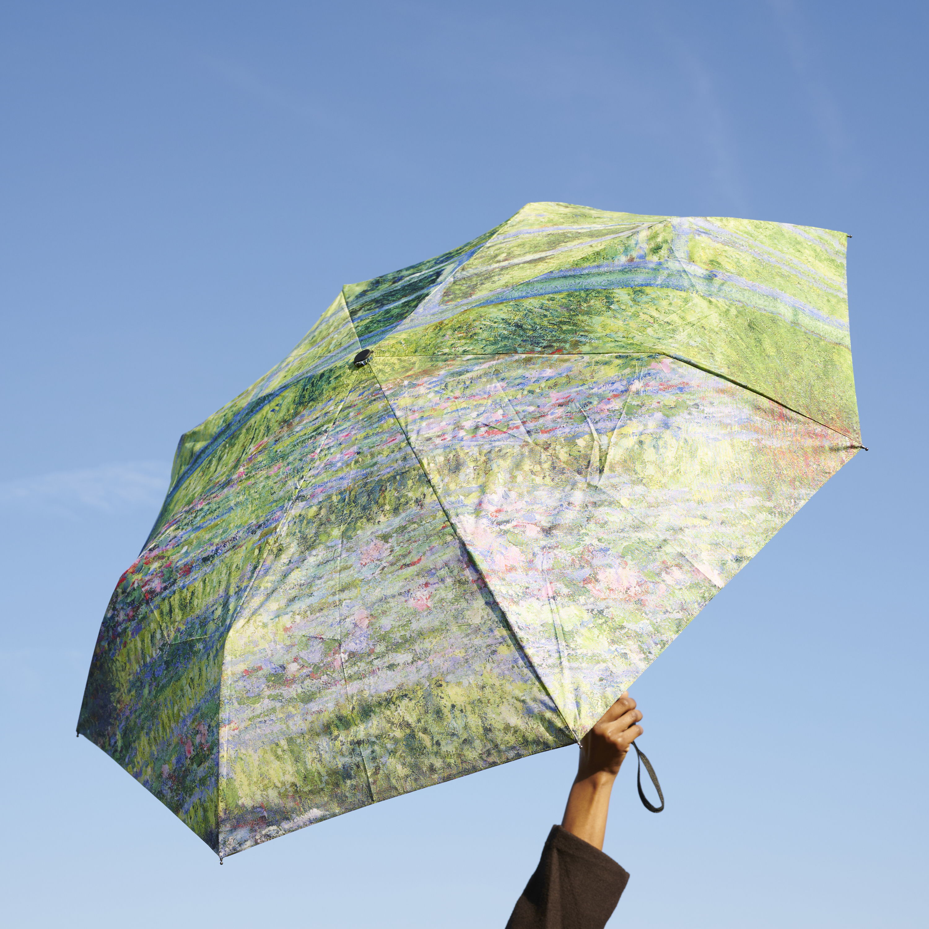 A hand holding a colorful umbrella against a clear blue sky.