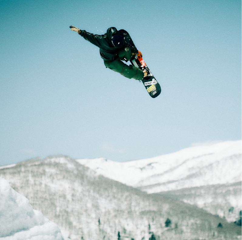 Snowboarder performing a jump against a snowy mountain backdrop.