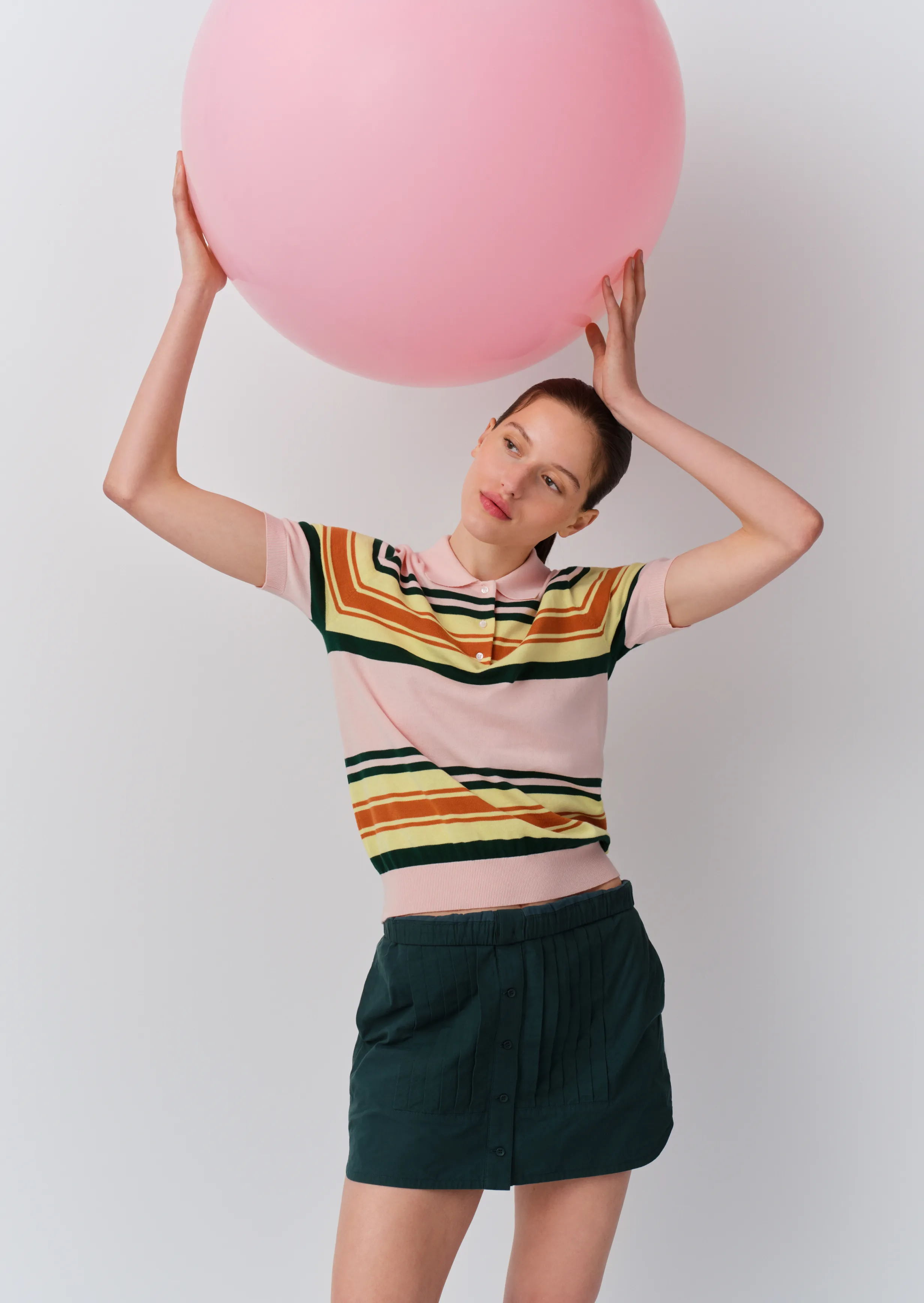 A woman holds a large pink balloon while wearing a colorful striped shirt.