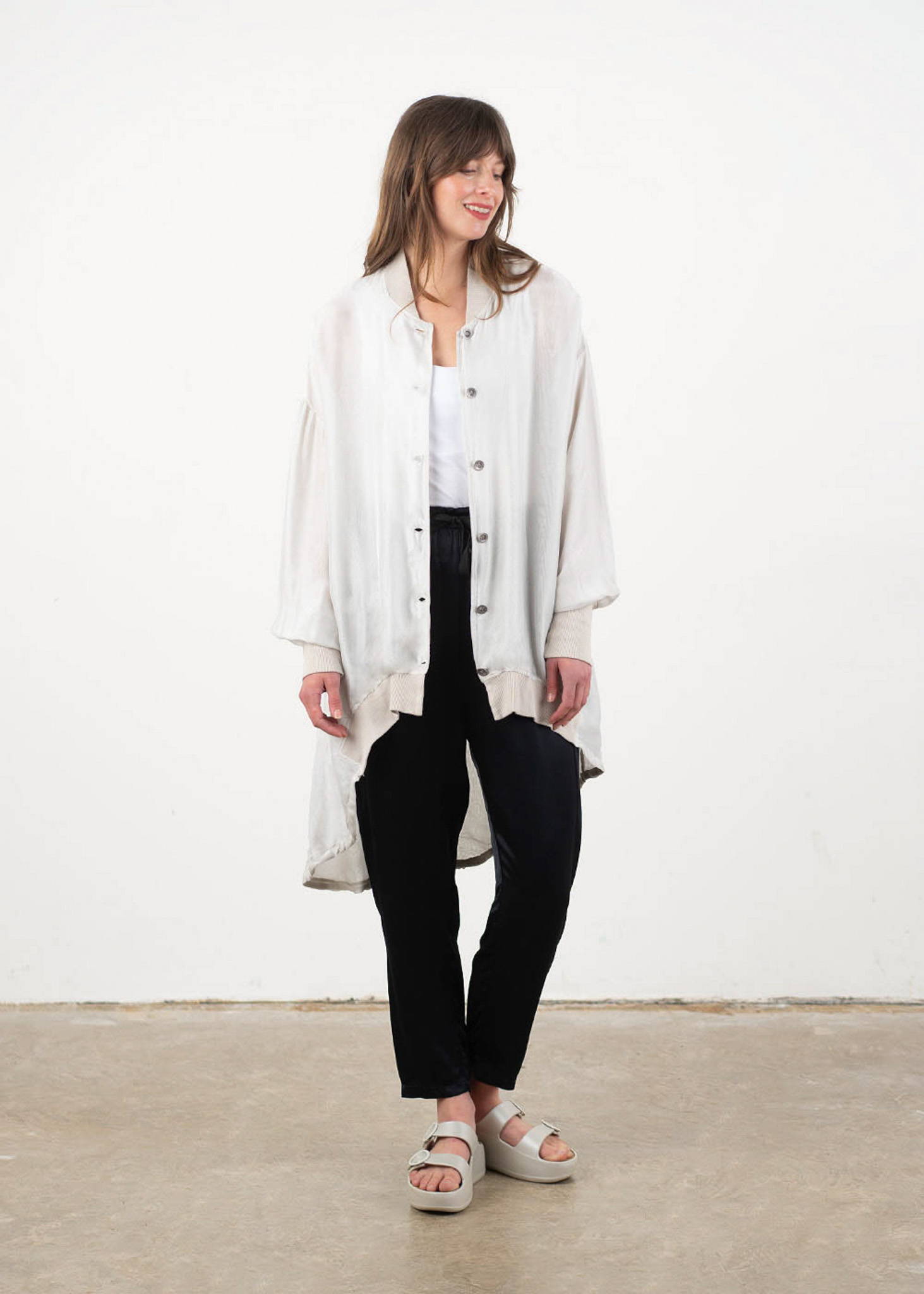A model wearing an off white oversized silk jacket with a white top, black trousers and white chunky platform slides.
