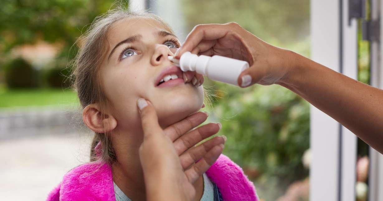 Child tipping her back as her mother gives her a dose of corticosteroid nasal spray to ease a stuffy runny nose from allergies